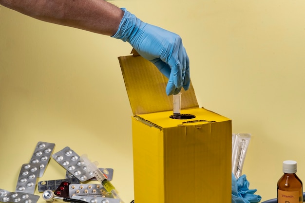 Foto caixa de descarte amarela para produtos contaminados ou infecciosos em um hospital ou em casa. mão colocando uma seringa