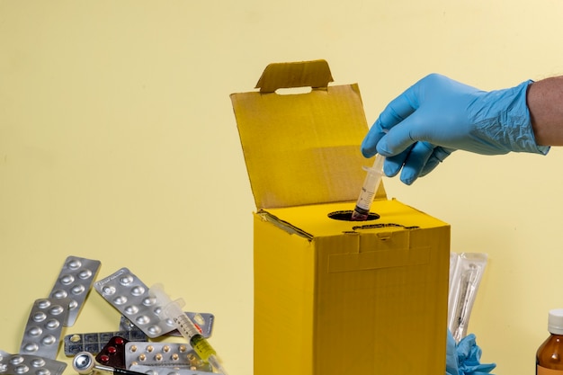 Foto caixa de descarte amarela para produtos contaminados ou infecciosos em um hospital ou em casa. mão colocando uma seringa