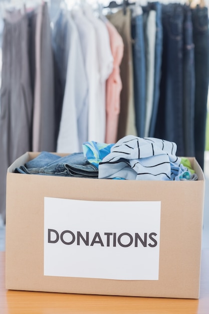 Foto caixa de doações cheia de roupas na frente do trilho de roupas