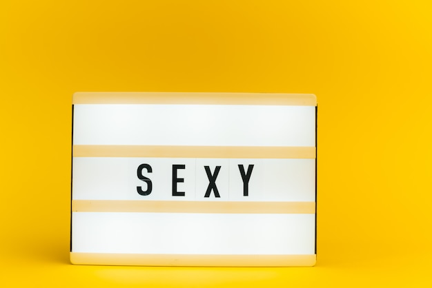 caixa de luz com texto, "SEXY", na parede amarela