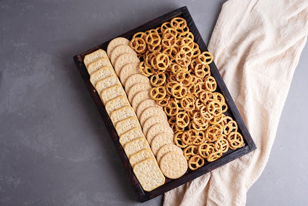 Caixa de madeira com biscoitos, biscoitos e mini pretzels salgados e têxteis em um fundo cinza de concreto, lanches de festa, close-up.