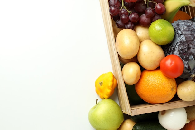 Caixa de madeira com diferentes vegetais e frutas na mesa branca