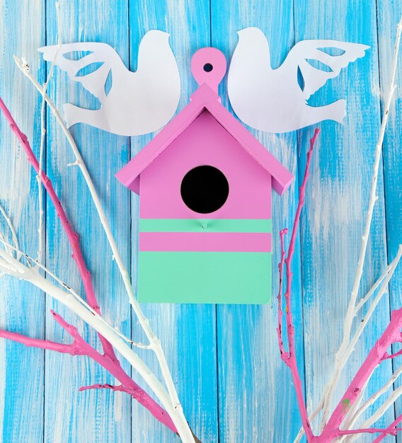 Caixa de nidificação decorativa com pássaros de papel e ramos de cor sobre fundo de madeira de cor