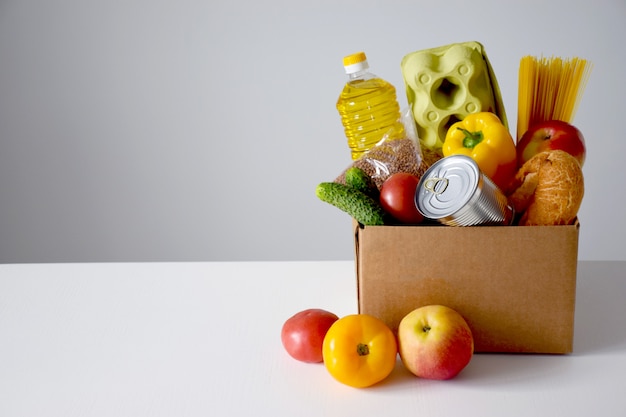 Caixa de papelão com alimentos, óleo, pão, ovos, tomate, maçã, pepino, lata, espaguete