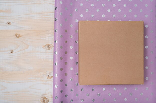 Caixa de papelão e papel de embrulho de bolinhas lilás, mesa de madeira, preparação para o feriado