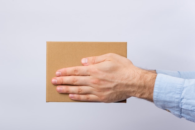 Caixa de papelão quadrada nas mãos masculinas. Entrega de encomendas. Vista lateral.