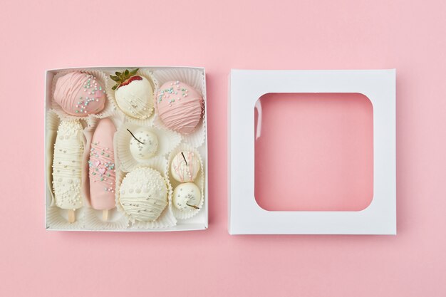 Caixa de presente aberta com frutas cobertas de chocolate branco e rosa estão no rosa