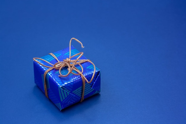 Caixa de presente azul amarrada com uma corda laranja em um fundo azul. copie o espaço.