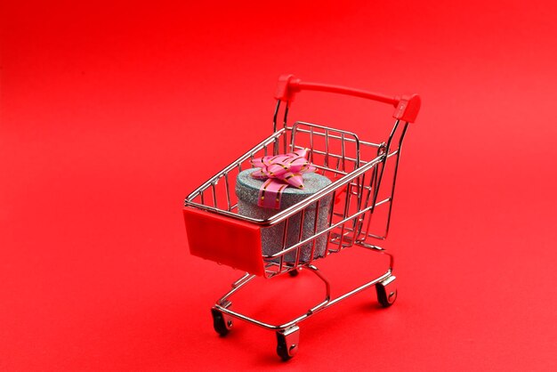 Caixa de presente azul com laço rosa em um carrinho de compras em um fundo vermelho