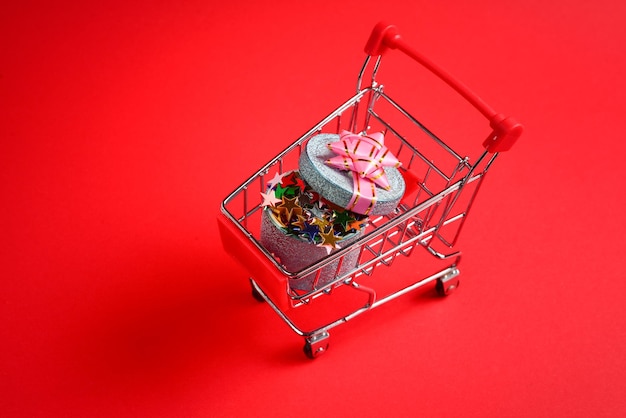 Caixa de presente azul com laço rosa em um carrinho de compras em um fundo vermelho