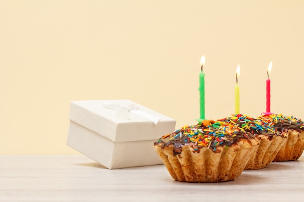 Caixa de presente branca e saborosos muffins de aniversário com esmalte de chocolate e caramelo, decorados com queima de velas festivas em fundo de madeira e bege. Conceito de feliz aniversário.