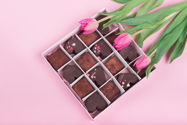 Caixa de presente com corações de doces de chocolate e tulipas em fundo rosa. Deserto para o Dia dos Namorados