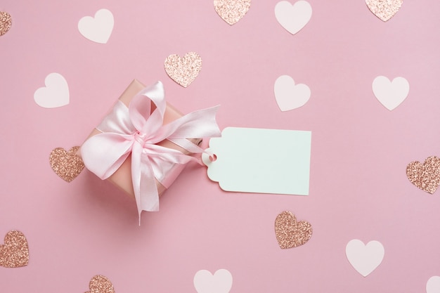 Caixa de presente com etiqueta de presente em branco sobre fundo rosa pastel com muitos corações. Composição do dia dos namorados. Vista superior, configuração plana.