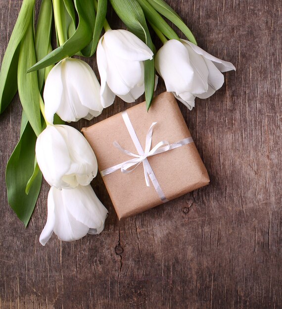 Caixa de presente com flores (tulipas brancas) sobre fundo de madeira rústica
