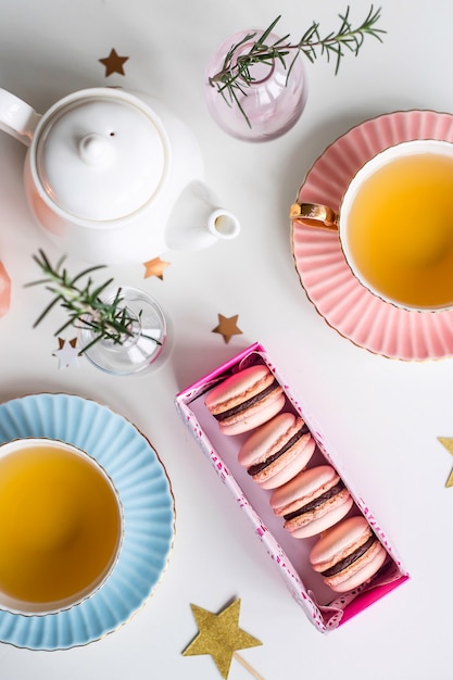 Caixa de presente com macaroons rosa entre xícaras vintage de chá verde, estrelas e pequenos vasos