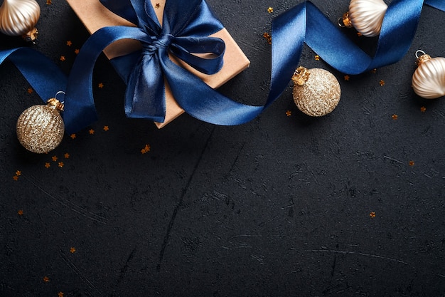 Caixa de presente de feriado ou presente com fita azul, confete dourado e enfeites de ouro sobre fundo preto. Cartão mágico de Natal. Decoração de Natal. Projeto de borda. Brincar. Vista do topo.