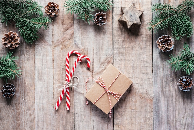 Caixa de presente de Natal com bastões de doces e galhos de pinheiros em fundo de madeira