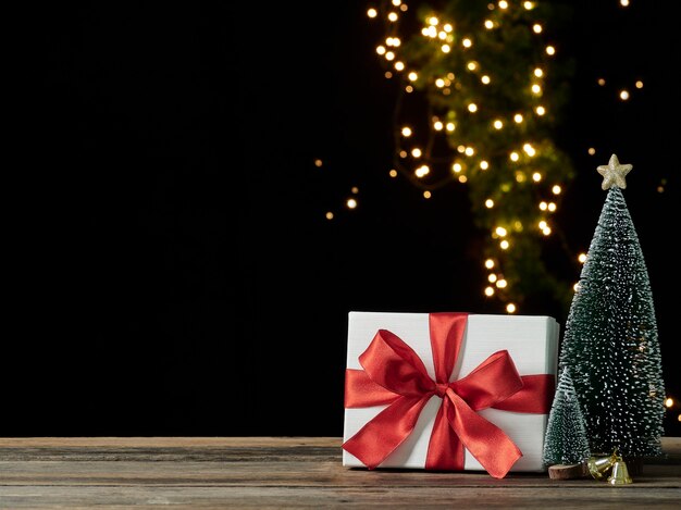 Caixa de presente de natal com enfeites em mesa de madeira contra luzes festivas borradas em fundo escuro, espaço para texto