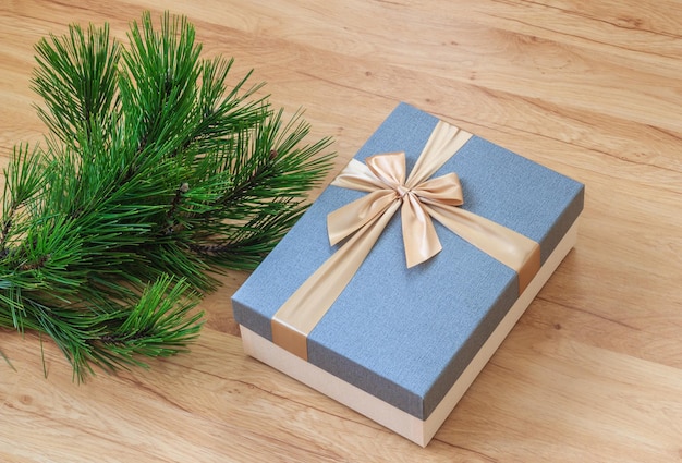 Caixa de presente de natal com fita de ouro elegante perto de galhos de pinheiro verde no chão de madeira
