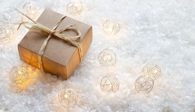 Caixa de presente de natal com fita de ráfia e luzes na vista superior de neve