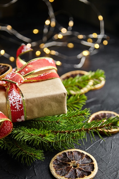 Caixa de presente de Natal com guirlanda de luz e galhos de pinheiro com frutas secas de laranja em fundo preto