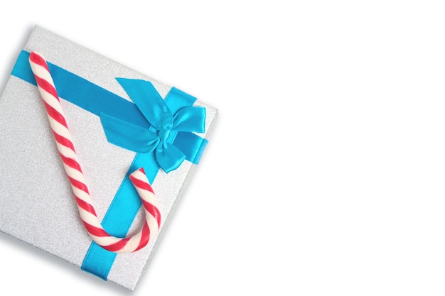 Caixa de presente de natal com laço azul e um doce vermelho e branco em bengala em fundo branco