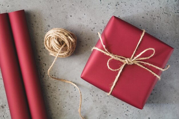 Caixa de presente de Natal de papel vermelho e um fio entre uma mesa cinza O conceito de embrulhar presentes Vista superior plana