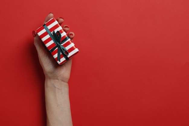 Caixa de presente de Natal em uma mão feminina sobre um fundo vermelho. Lugar para texto. Vista do topo.