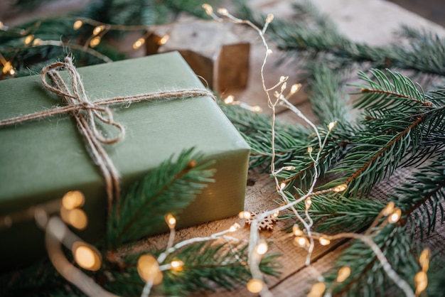 Caixa de presente de Natal embrulhada em papel kraft verde e decorada com galho de pinheiro no fundo festivo do ano novo