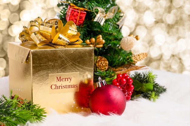 Caixa de presente de ouro brilhante com palavra Feliz Natal com bola de decoração vermelha