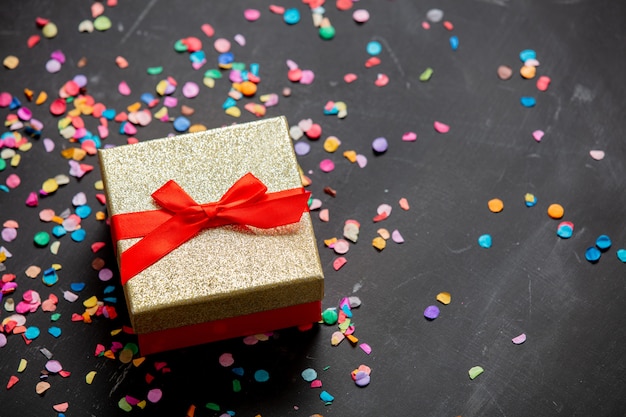 Caixa de presente dourada com fita vermelha e confetes ao redor