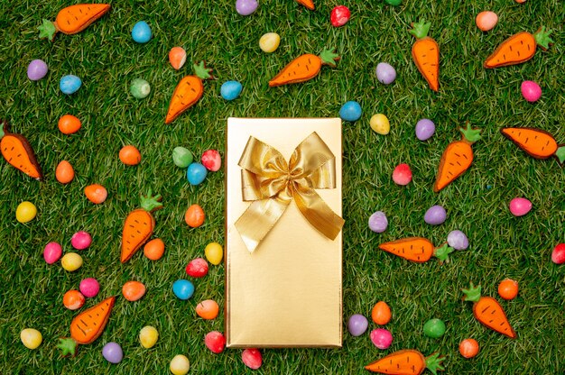 Caixa de presente dourada e ovos de Páscoa com biscoitos de cenoura na grama verde
