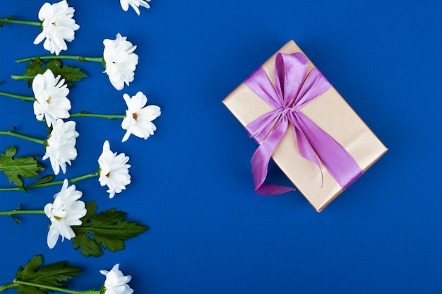 Caixa de presente e flores na mesa azul. Cartão para aniversário, mulher ou dia das mães. Vista do topo