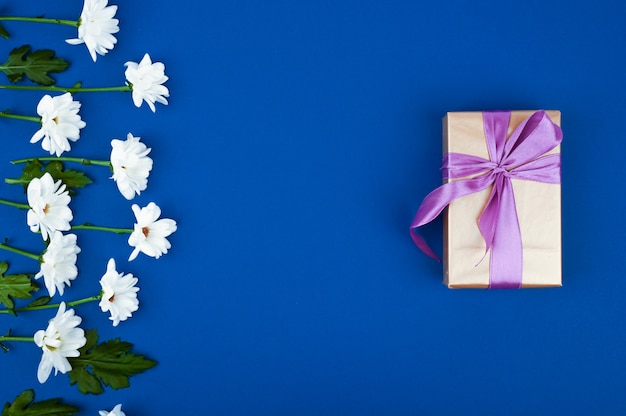 Caixa de presente e flores na mesa azul. Cartão para aniversário, mulher ou dia das mães. Vista do topo