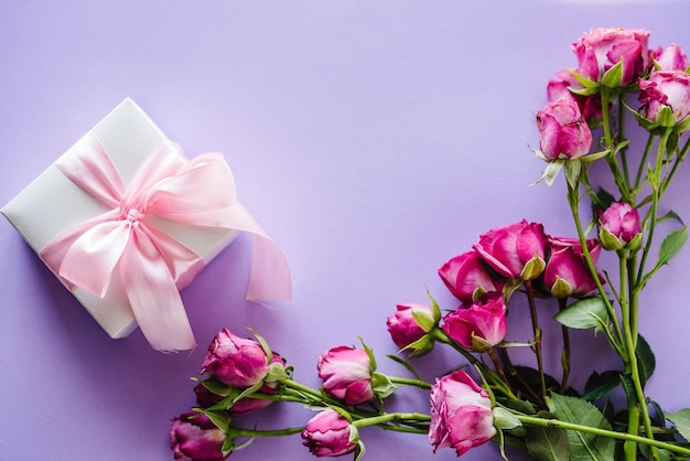 Caixa de presente e rosas cor de rosa no fundo violeta cartão postal espaço para mensagem de texto conceito de flores cartão de felicitações para dia dos namorados dia das mães das mulheres páscoa feliz aniversário convite de casamento