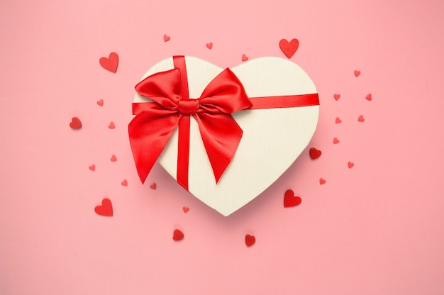 Caixa de presente em forma de coração com um laço vermelho na parede rosa.