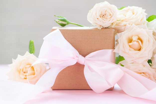 Caixa de presente embrulhada em papel pardo com rosas em fundo rosa. Cartão de felicitações.