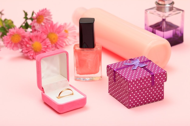 Foto caixa de presente, flores, frascos com esmalte, xampu e perfume, anel de ouro em uma caixa em um fundo rosa. cosméticos e acessórios femininos.