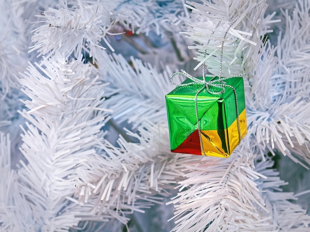 Foto caixa de presente pequena colorida pendurada na árvore de natal branco