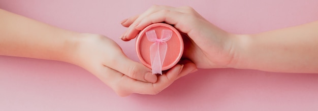 Foto caixa de presente rosa redonda nas mãos das mulheres em um fundo rosa. conceito festivo para dia dos namorados, dia das mães ou aniversário