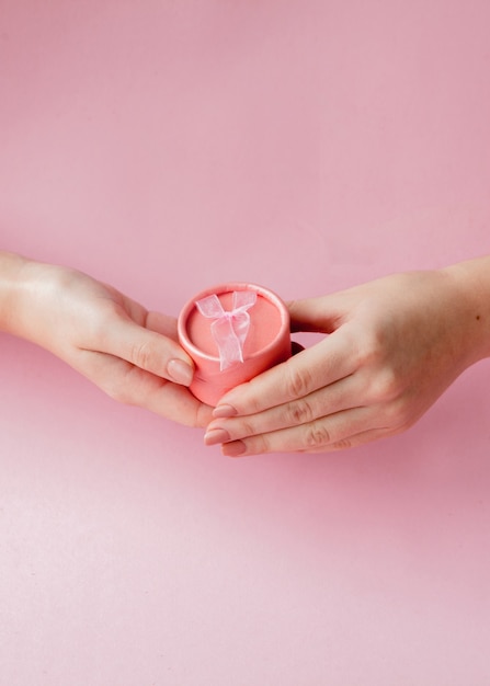 Caixa de presente rosa redonda nas mãos de mulheres em um fundo rosa. conceito festivo para o dia dos namorados, dia das mães ou aniversário.