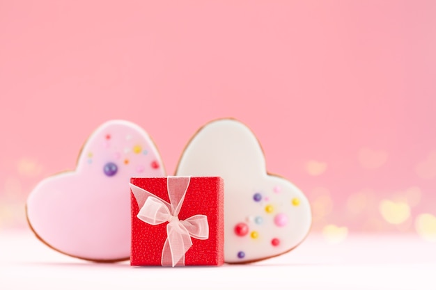 Caixa de presente vermelha com dois corações em forma de pão de mel para o dia dos namorados, dia das mães ou aniversário em fundo rosa.