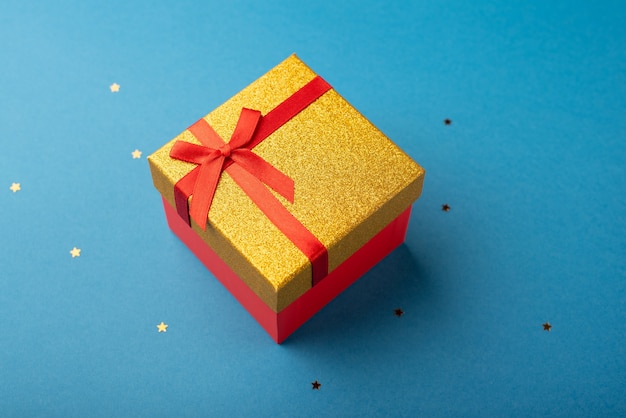 Caixa de presente vermelha e dourada com uma fita vermelha em um fundo azul com estrelas
