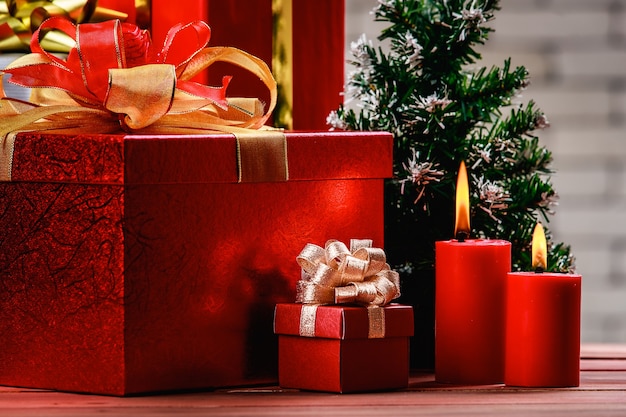 Caixa de presente vermelha festiva e velas vermelhas iluminar na placa de madeira natural decorar com árvore de Natal, fundo de parede de tijolo branco turva.