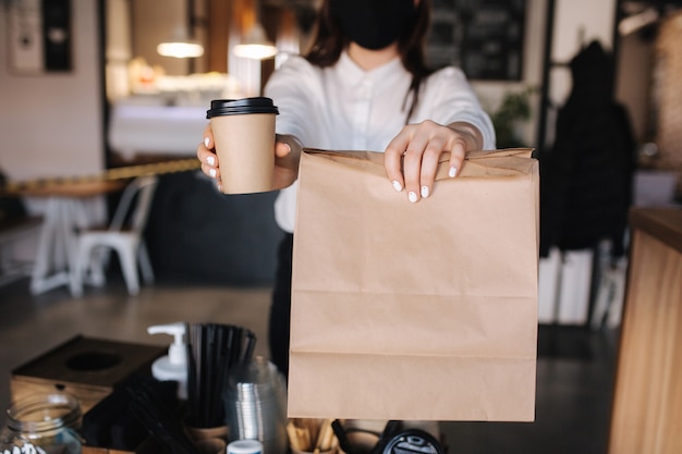 Caixa feminina com máscara facial servindo café e comida para a loja do cliente aberta após uma mulher de bloqueio