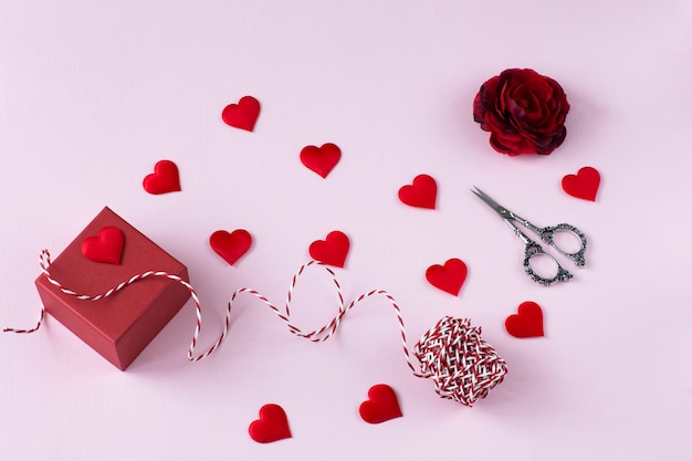 caixa vermelha com um presente, uma fita para embrulho, tesoura e corações vermelhos
