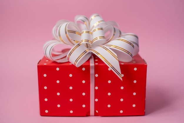 Caixa vermelha de presente com bolinhas brancas com um laço branco sobre fundo rosa