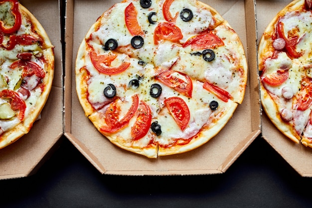 Caixas abertas com gostosa comida italiana gostosa fatiada três pizzas em fundo preto