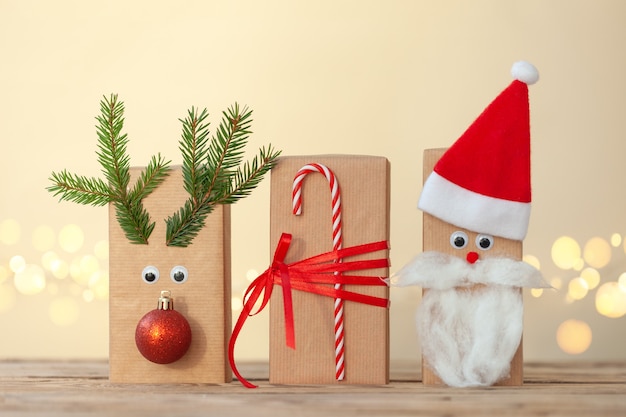 Caixas de Natal artesanais embrulhadas em papel de presente artesanal decorado com chapéu de Papai Noel e veados em fundo de madeira com bokeh cintilante. Conceito de ano novo