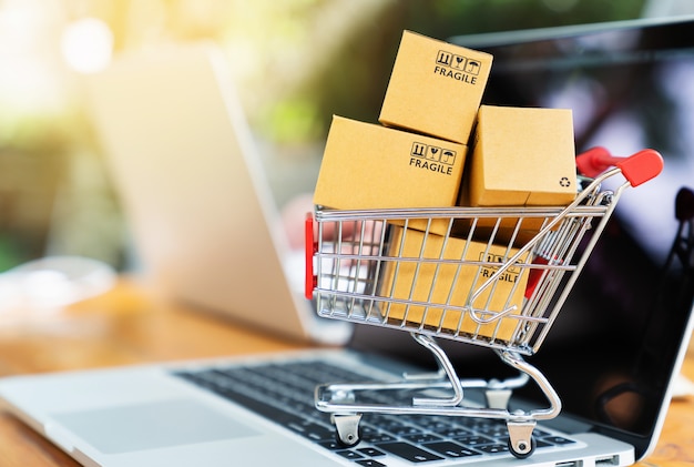 Caixas de pacote no carrinho com o computador portátil para o conceito de compras on-line